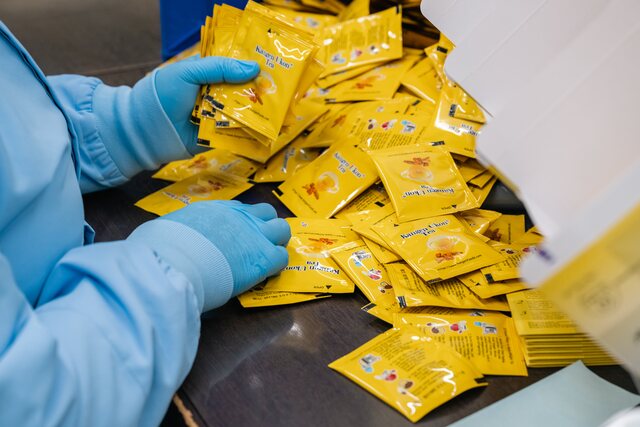 A gloved worker packing Kangen Ukon Tea sachets into a carton