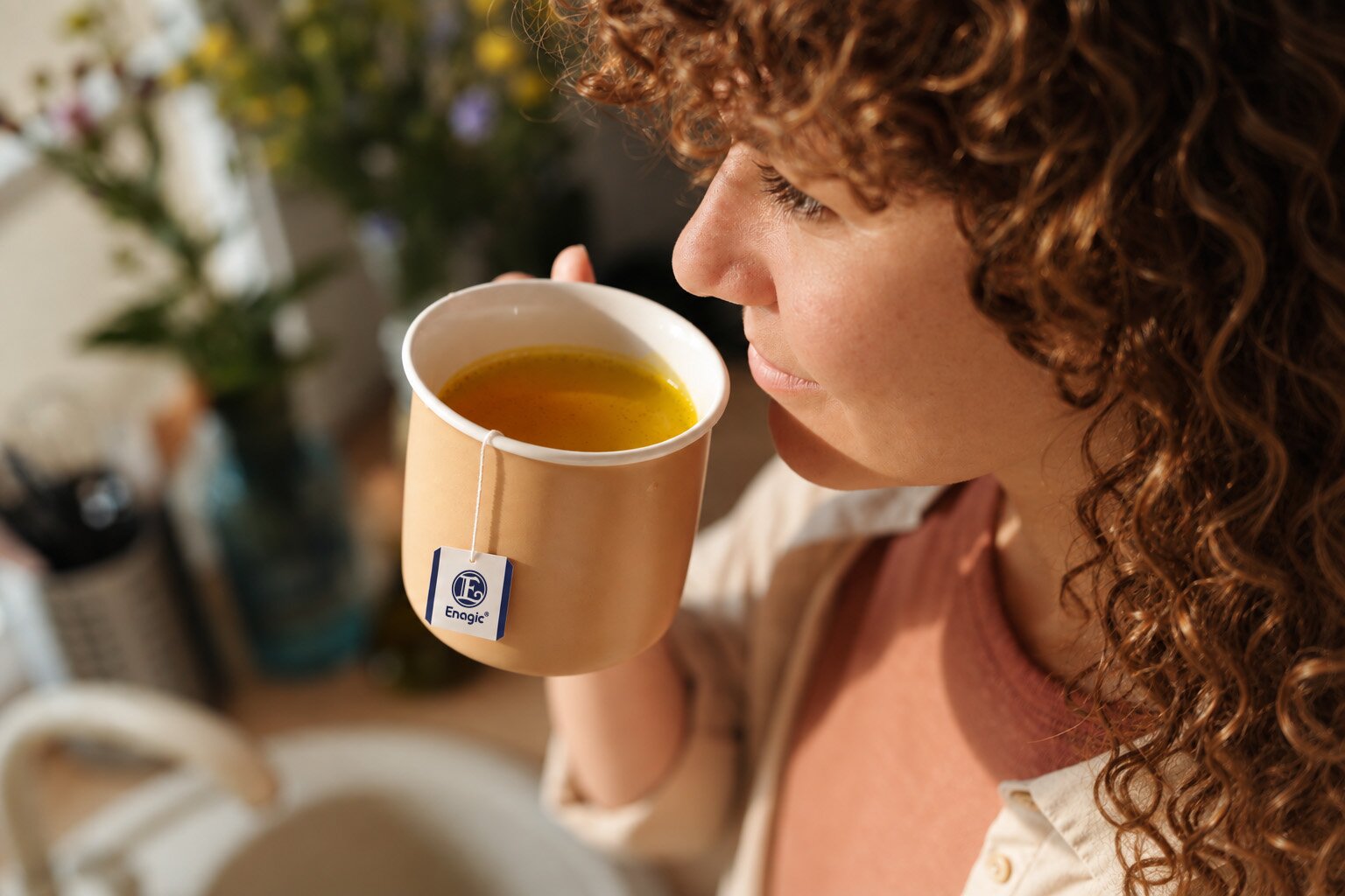 A woman raising a mug of brewed Kangen Ukon Tea, the Enagic tea bag tag hanging over the rim